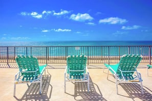 Drie groene stoelen gericht op een strand met een heldere lucht.