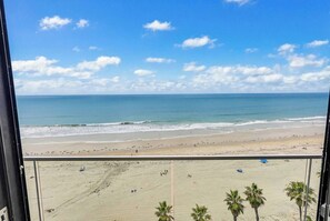 Vista al mar desde un balcón, con palmeras y cielo despejado.