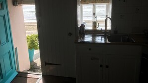 Una cocina con ventana que da a la playa, un fregadero y armarios.