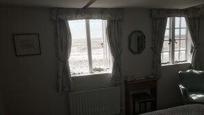 Un dormitorio con una cama grande, una silla, una mesita y una ventana con cortinas.