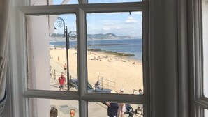 Vista a través de una ventana que muestra una playa, con gente y un cielo despejado.