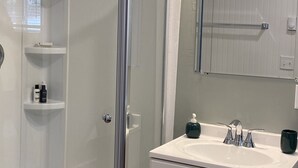 Un baño con cabina de ducha de vidrio, un lavabo blanco con espejo arriba y un mueble blanco debajo.