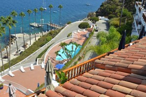 A curved road leading to a pool area with palm trees and a view of the sea. - Cozy 1bd Oceanfront balcony view and golf cart (Avalon)