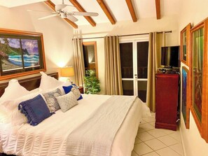 A hotel room with a bed, a ceiling fan, a television, and a sliding glass door leading to a balcony. - Cozy 1bd Oceanfront balcony view and golf cart (Avalon)