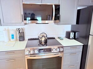 A kitchen with a stove, microwave, oven, and a kettle.
