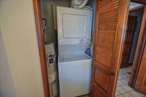A compact laundry area with a washing machine and dryer stacked vertically. - Hamilton Cove Oceanfront view 2bd with golf cart (Avalon)