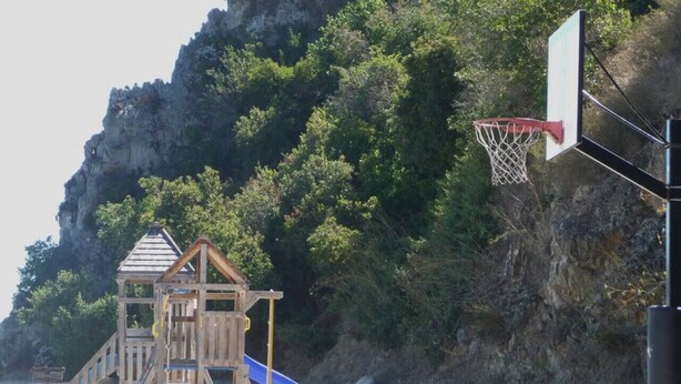 A playground with a wooden play structure, a blue slide, and a basketball hoop.