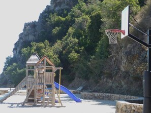 A playground with a wooden play structure, a blue slide, and a basketball hoop. - Hamilton Cove Oceanfront view 2bd with golf cart (Avalon)
