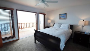 A bedroom with a bed, two bedside tables with lamps, a ceiling fan, and a balcony door.