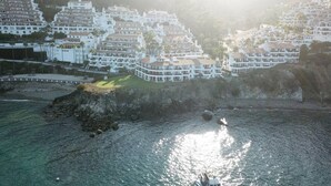 A coastal town with multi-story buildings, a rocky shoreline, and a clear view of the sea.