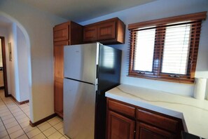 A kitchen with wooden cabinets, a stainless steel refrigerator, and a window with blinds. - Hamilton Cove Oceanfront view 2bd with golf cart (Avalon)