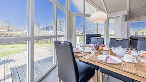 Un coin repas avec une table dressée pour quatre personnes, de grandes fenêtres et une vue sur le paysage environnant.