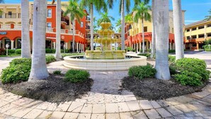 Une cour intérieure avec une fontaine centrale, entourée de palmiers et d’immeubles dotés de balcons.