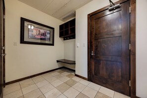 A hallway with a wooden door, a framed picture on the wall, and a tiled floor.