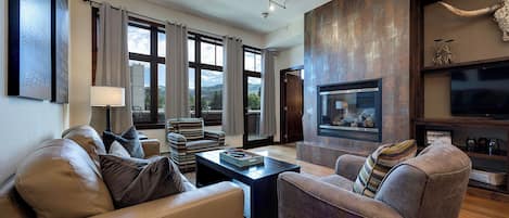 A modern living room with leather sofas, a fireplace, and a large window offering a view of the outdoors.