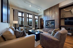 A modern living room with leather sofas, a fireplace, and a large window offering a view of the outdoors.