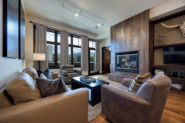 A modern living room with leather sofas, a fireplace, and a large window offering a view of the outdoors.