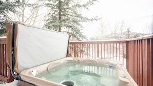 A hot tub with a glass cover, surrounded by a wooden deck and snow-covered trees.