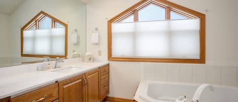 Un baño moderno con tocador doble, muebles de madera, un espejo grande y una bañera independiente.
