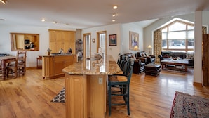 A spacious kitchen with wooden cabinets and a granite countertop, a dining area with a wooden table and chairs, and a living room with a sofa and a coffee table.