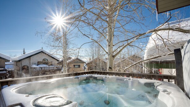 A hot tub with a control panel, surrounded by snow-covered trees and buildings.