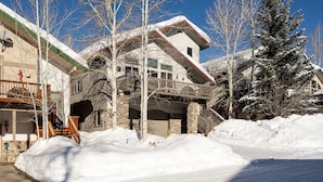 A snow-covered building with a stone facade, a balcony, and a ski lift visible in the background.