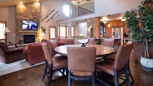 A spacious living room with a fireplace, a dining area with a round table, and a kitchen with wooden cabinets.