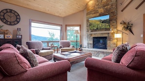 A spacious living room with a stone fireplace, large windows, and a cozy seating area with red upholstered sofas.