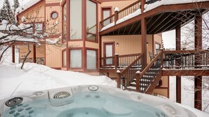 A hot tub outside a wooden building with a balcony and stairs.