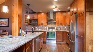 Una cocina con armarios de madera, un refrigerador de acero inoxidable, horno empotrado y encimera de granito.