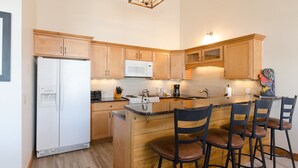 Une cuisine moderne avec des meubles en bois, un four à micro-ondes encastré, une cuisinière et un coin bar avec des tabourets.