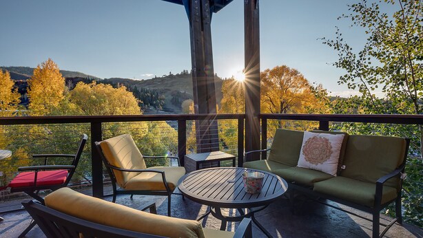 Un espacio de estar techado al aire libre con una mesa y sillas, con vistas a un paisaje de árboles y colinas.