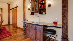 Una cocina con armarios de madera, encimera de granito, pileta y un taburete de bar.