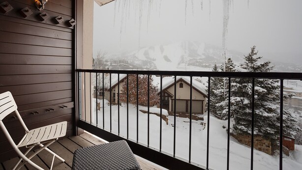 Ein Balkon mit Blick auf eine verschneite Landschaft, ein weißer Klappstuhl und eine Wandleuchte.