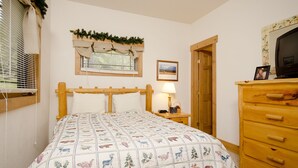 A bedroom with a wooden bed, a bedside table with a lamp, a dresser, and a window with blinds. - SCK765 | Great Location | Free City Bus | Close to Slopes (Steamboat Springs)
