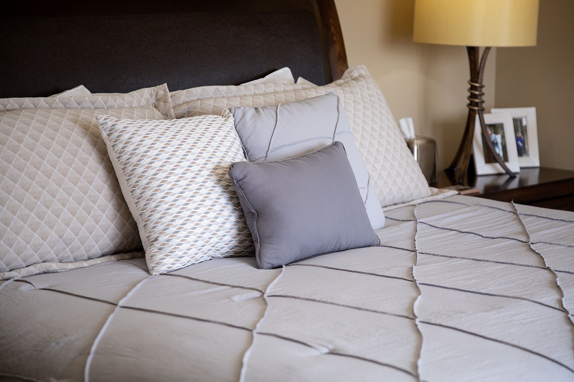 Una cama con cabecera acolchada, varios almohadones y una lámpara de noche.
