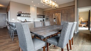A modern kitchen with wooden cabinets, a stainless steel refrigerator, and a dining area with a wooden table and grey upholstered chairs. - SL300 | Modern Penthouse | Views | Pool | Hot Tub | 100 Yds to Lift (Steamboat Springs)