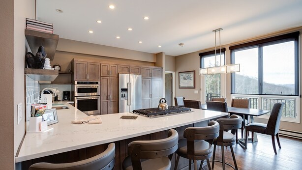 A modern kitchen with a large island, bar stools, and a dining area with a view. - SL300 | Modern Penthouse | Views | Pool | Hot Tub | 100 Yds to Lift (Steamboat Springs)