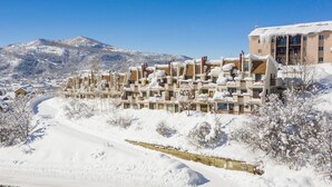 Uma área residencial coberta de neve, com edifícios altos, céu limpo e uma montanha ao fundo.