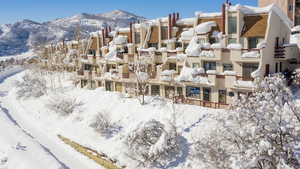 Um hotel com vários andares, com varandas cobertas de neve, rodeado por árvores e montanhas cobertas de neve ao fundo.