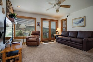 A living room with a brown leather chair, a brown leather sofa, a ceiling fan, and a large window with blinds. - SW202 | Updated Condo | Great Views | Close to Base Area | A/C (Steamboat Springs)