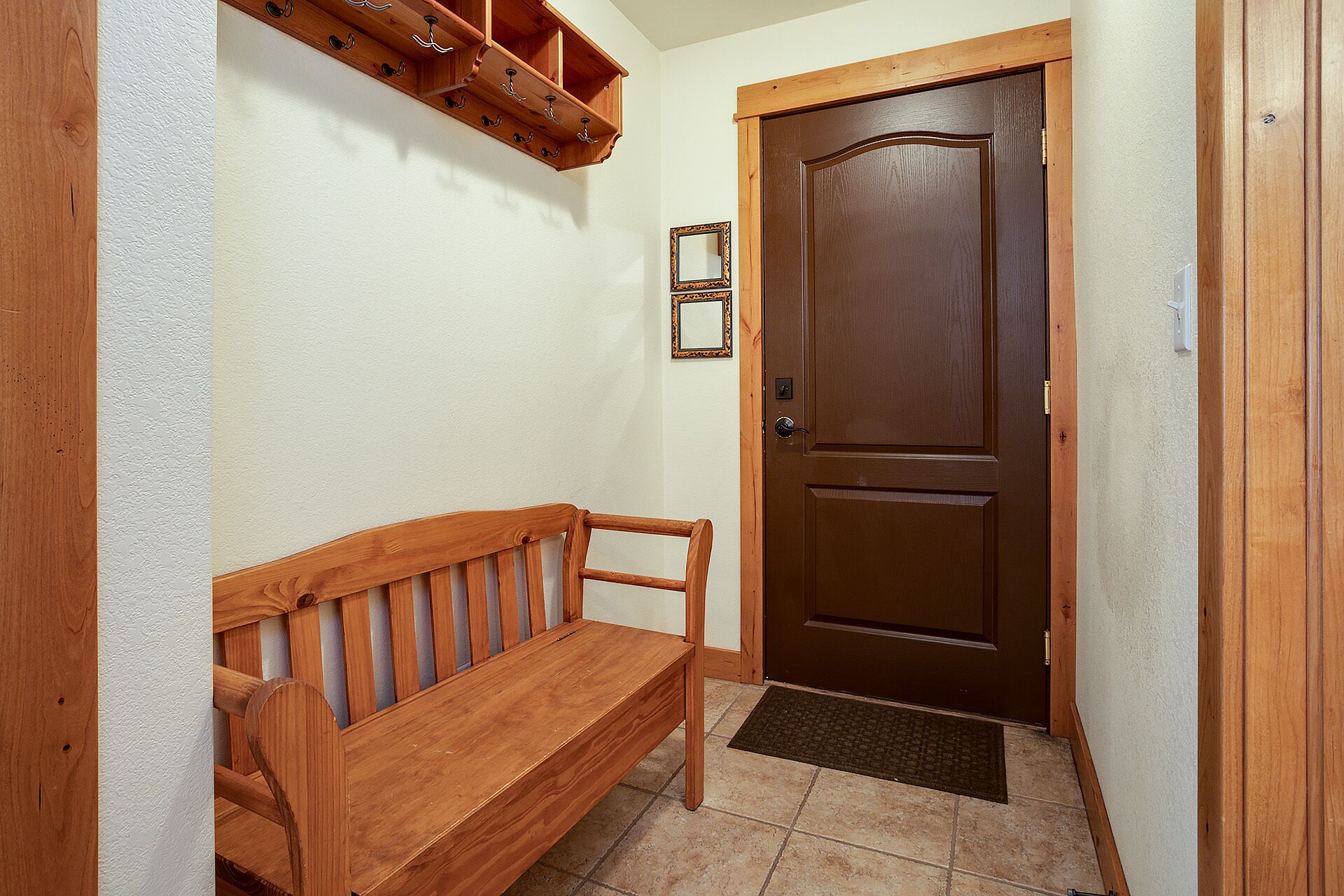Un banc en bois, une porte marron et un porte-manteau fixé au mur dans un couloir.