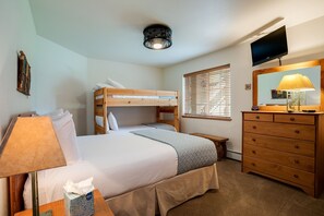 A bedroom with a bunk bed, a dresser, a television, and a lamp.