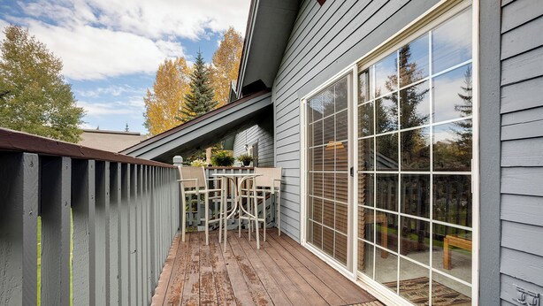 A covered patio with a wooden deck, a white outdoor table and chairs, and a large sliding glass door leading to a backyard. - V1421 | Private Garage | Hot Tub | Free City Bus | 5 Minutes to Base Area (Steamboat Springs)