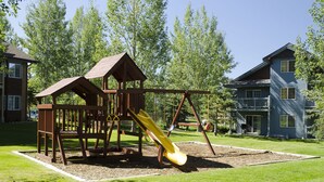 A playground with a slide and climbing structures, surrounded by a well-maintained lawn and trees. - V1421 | Private Garage | Hot Tub | Free City Bus | 5 Minutes to Base Area (Steamboat Springs)