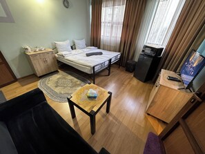 A compact hotel room with a bed, a small desk, a TV, a wardrobe, and a window with curtains. - ALEM HOTEL (Yerevan)