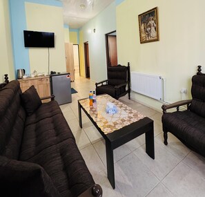 A living room with a sofa, armchair, coffee table, TV, radiator, and a painting on the wall. - ALEM HOTEL (Yerevan)
