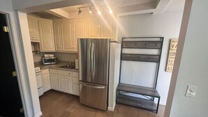 Una cocina compacta con armarios blancos, un refrigerador de acero inoxidable, horno empotrado y un banco de madera.