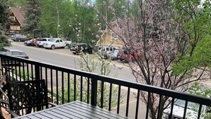Una terraza de madera con una mesa y banca de metal, con vistas a un estacionamiento y árboles.