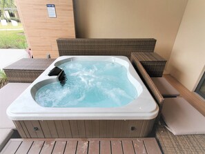 A hot tub with a wooden exterior, surrounded by wicker furniture and a wooden deck.